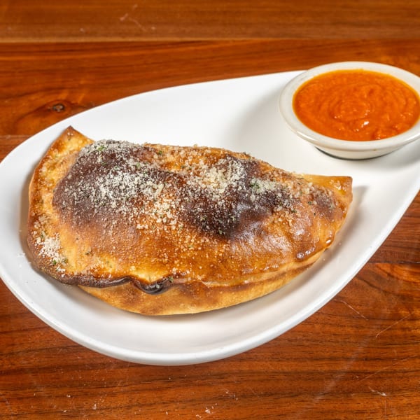A golden-brown calzone sprinkled with Parmesan cheese, served with a side of marinara sauce.