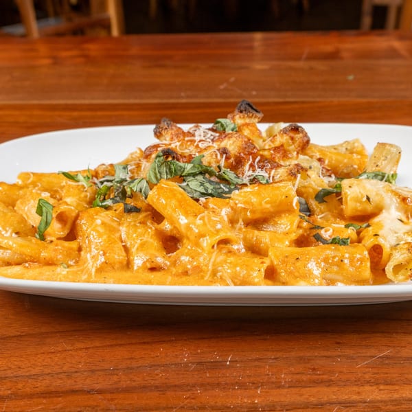 Napoli's baked ziti with creamy orange sauce, melted cheese, and fresh basil on a white plate.