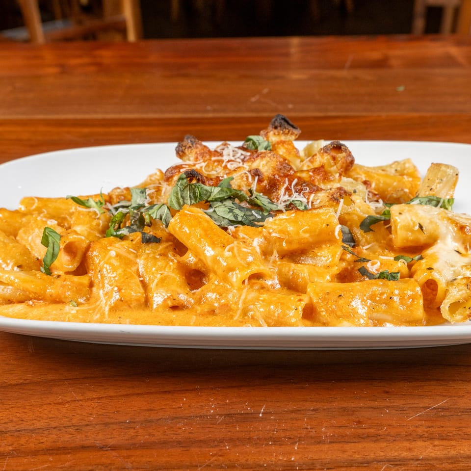 Napoli's baked ziti with creamy orange sauce, melted cheese, and fresh basil on a white plate.