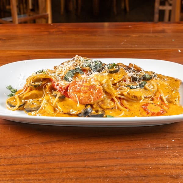 A plate of creamy orange pasta with mushrooms, tomatoes, and basil on a wooden table.