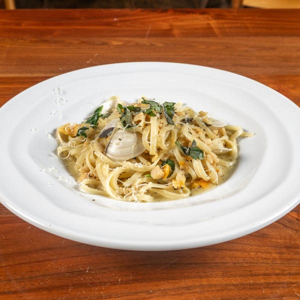 Linguine alle vongole with clams, fresh basil, and grated cheese on a white plate.