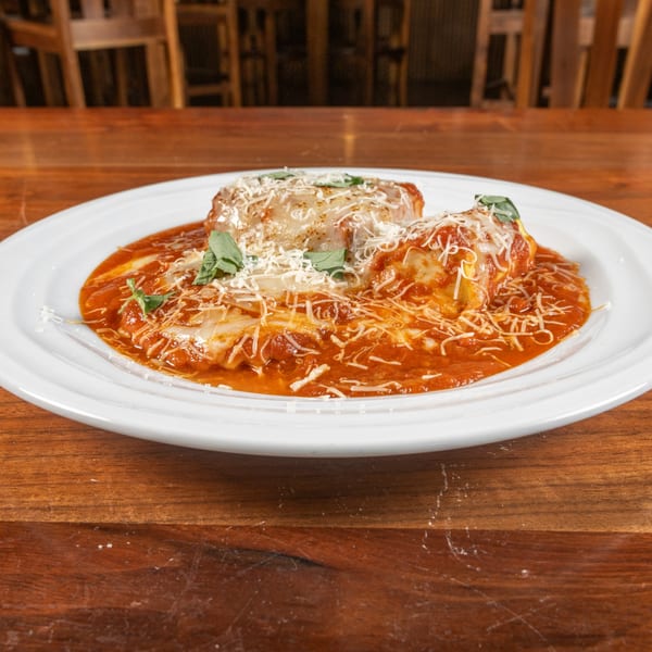 Two baked manicotti pasta rolls covered in red sauce, parmesan cheese, and basil on a white plate.