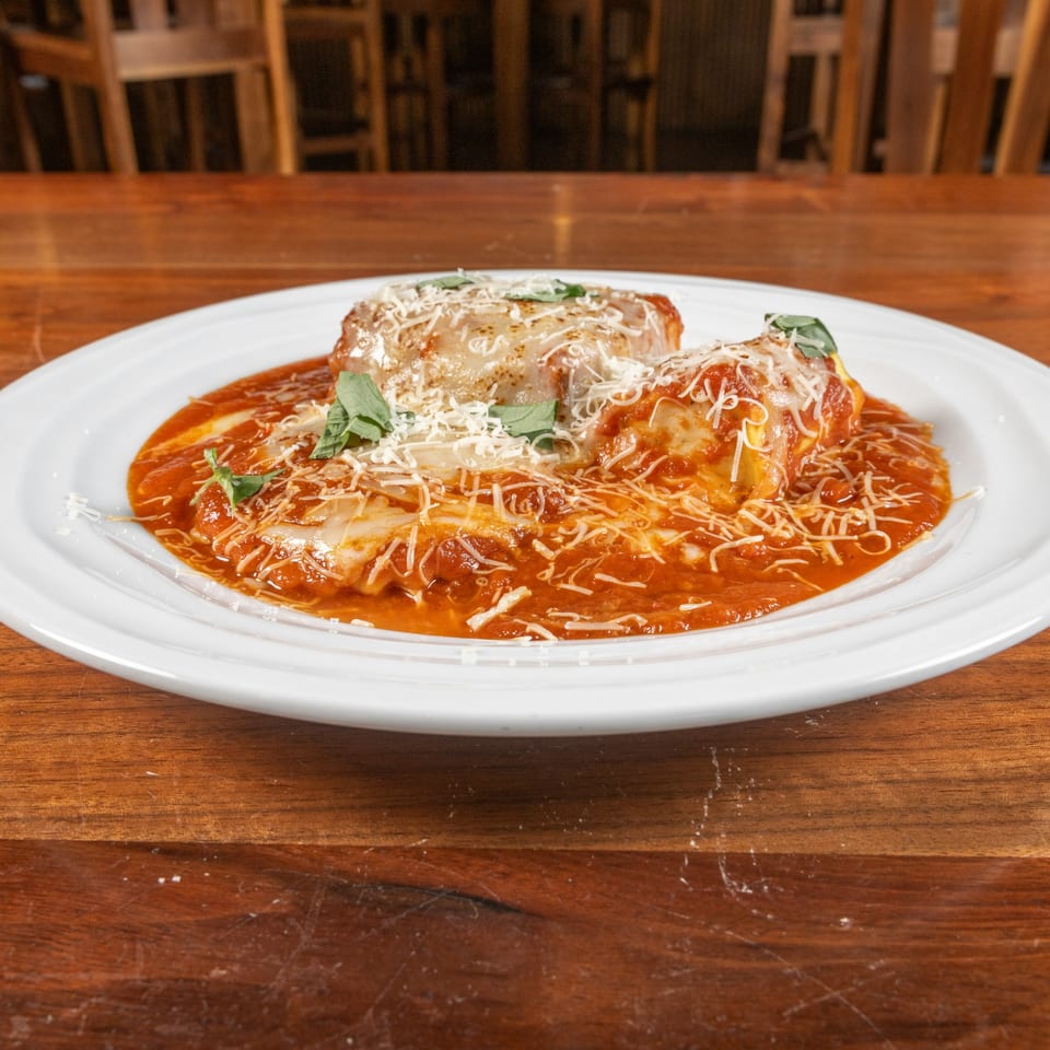 Two baked manicotti pasta rolls covered in red sauce, parmesan cheese, and basil on a white plate.