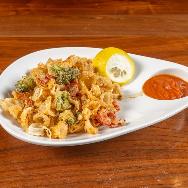 Fried calamari and vegetables with a lemon wedge and red dipping sauce on a white plate.